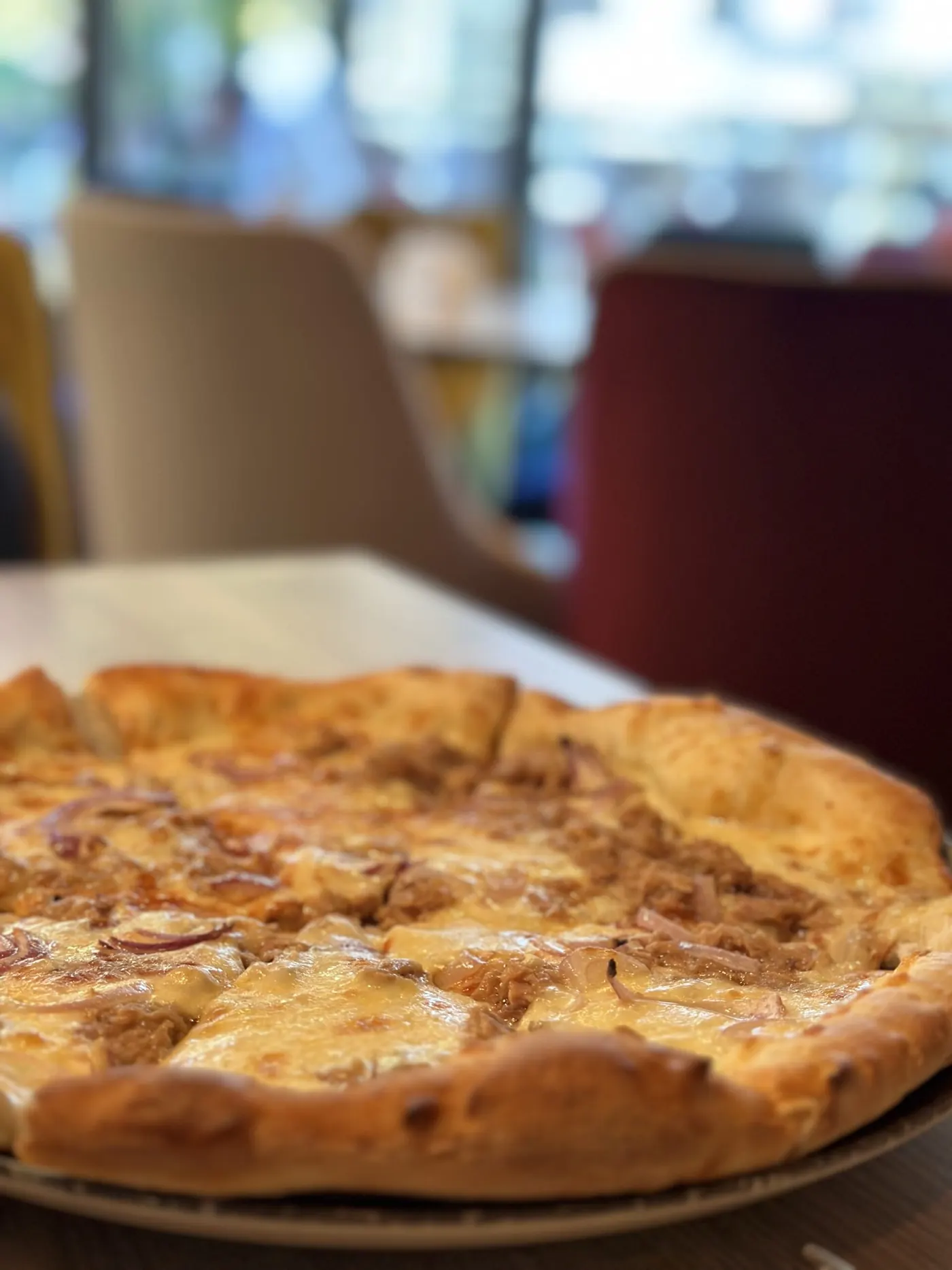 Pizza cu ton și ceapă roșie, tăiată felii, pe o masă din salonul restaurantului.