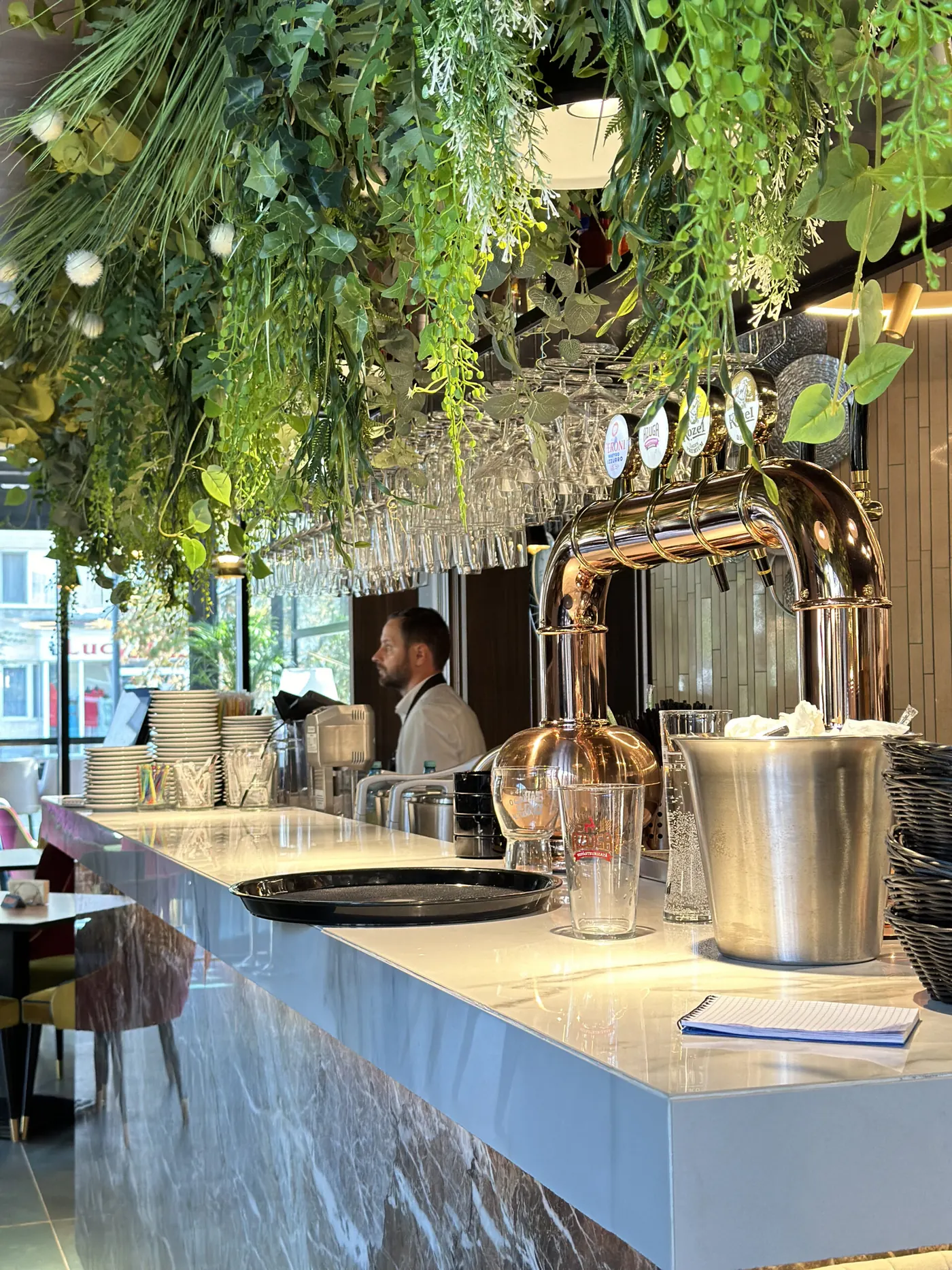 Barul restaurantului Pergola, cu pahare suspendate și o boltă de verdeață deasupra tejghelei de marmură.